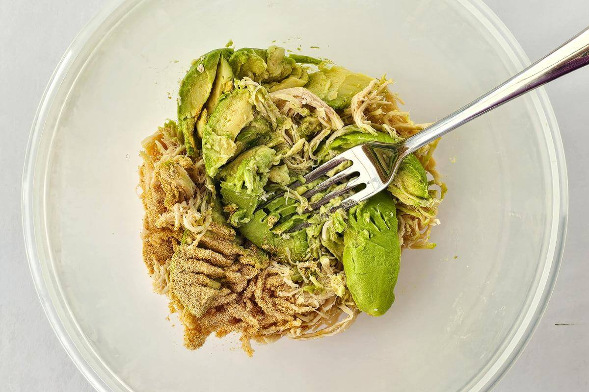 Ingredients for making avocado chicken salad mashed together in a bowl.