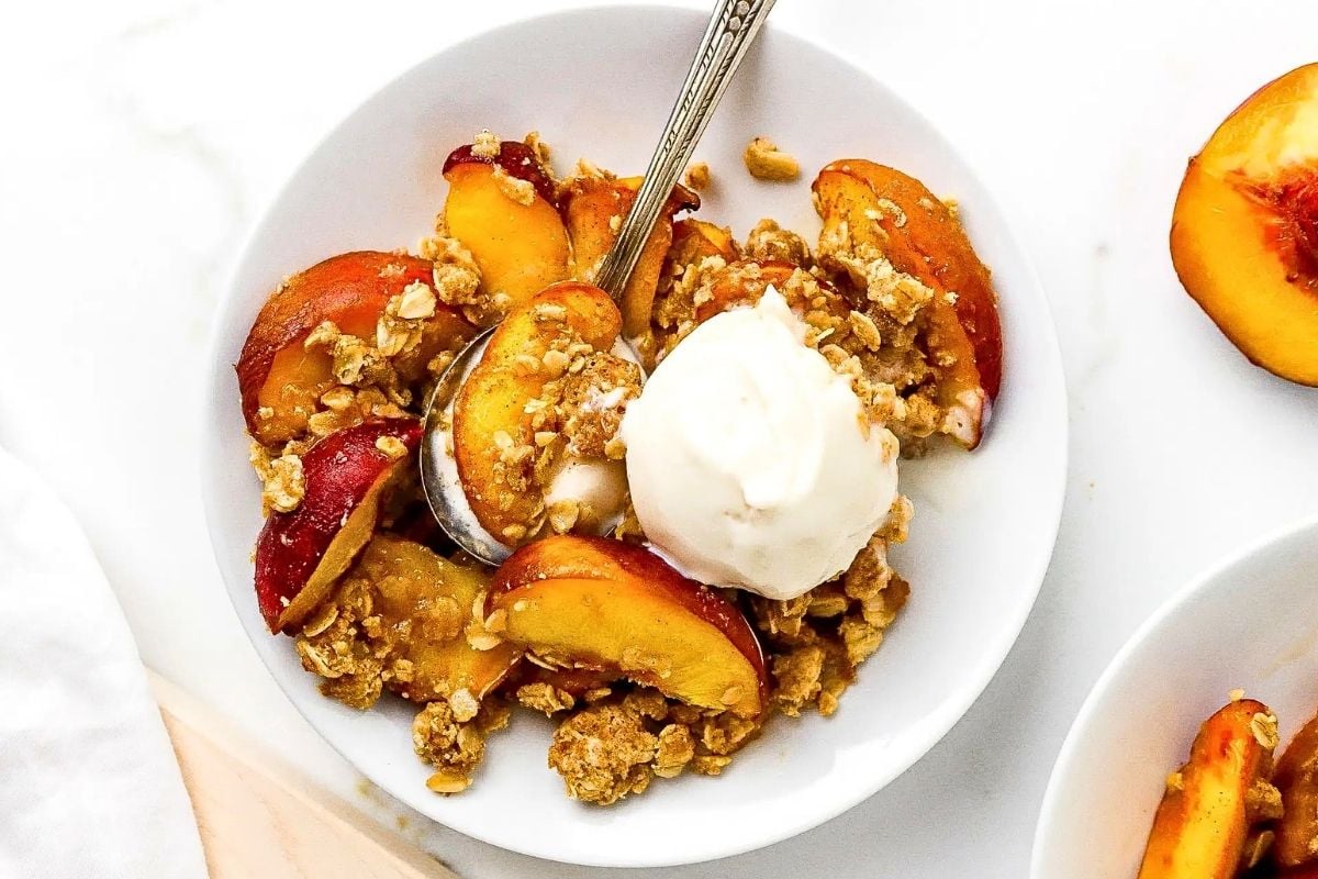 Air Fryer Peach Crisp in a white plate with a spoon on it. 