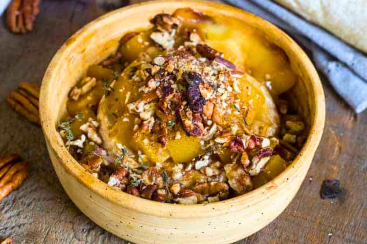 Baked Brie with Peaches, Pecans, Herbs and Honey in a small wooden bowl.