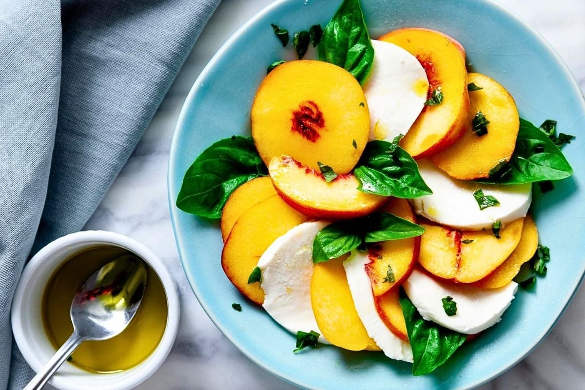 Peach Caprese Salad in a blue plate with a small bowl beside it. 