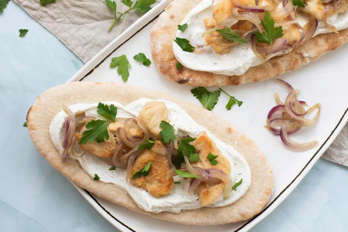 Two pitas topped with chicen and yogurt.