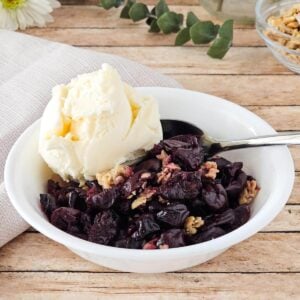 A bowl of gluten free cherry crisp with ice cream on top.