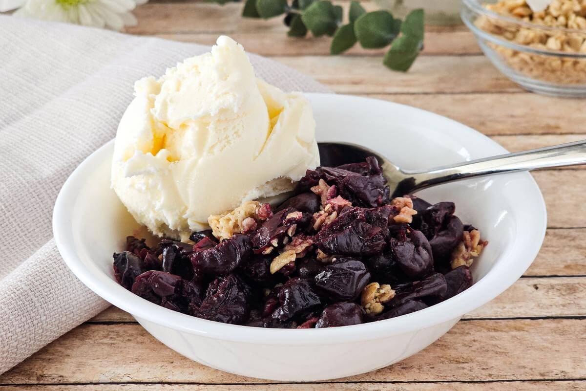 A bowl of gluten free cherry crisp with ice cream on top.