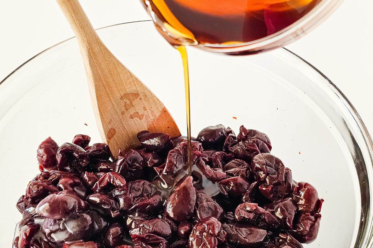 Maple syrup being poured into a glass bowl filled with cherries.