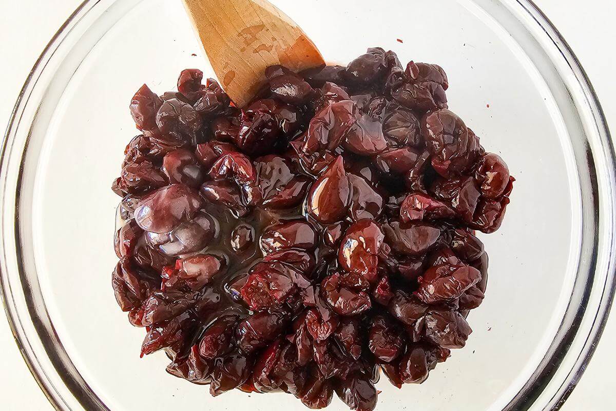 A wooden spoon mixing cherries in a glass bowl.