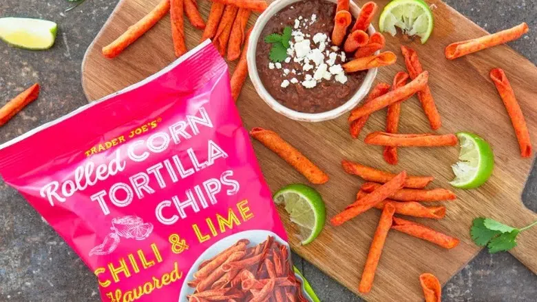 Trader Joe's Chili & Lime Flavored Rolled Corn Tortilla Chips on a wooden board with a bowl of dip and some lime wedges