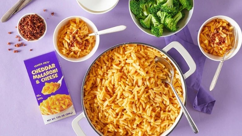 box of Trader Joe's  Cheddar Macaroni & Cheese next to a pot and two bowls of macaroni and cheese and a bowl of broccoli