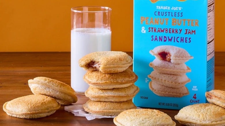 box of Trader Joe's Crustless Peanut Butter & Strawberry Jam Sandwiches pictured along with piles of the sandwiches and a glass of milk